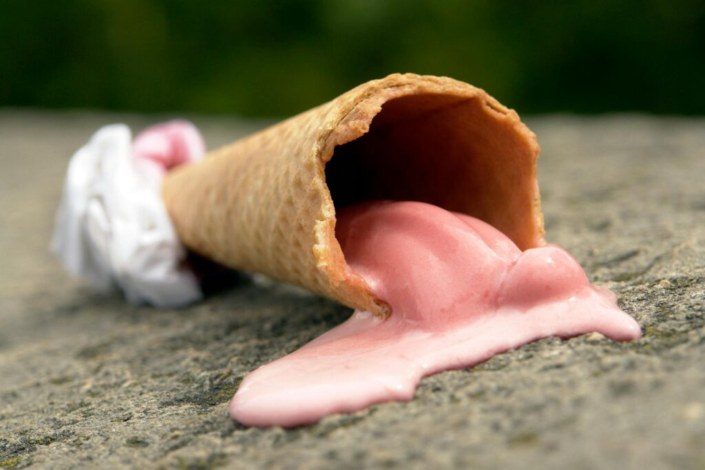 Think Before You Drink: 5 Guilt-Free Behavioral Science Hacks for Hydration 1 an ice cream cone, partially wrapped in a napkin lays on the sidewalk, the strawberry ice cream melting and dripping out of the cone.