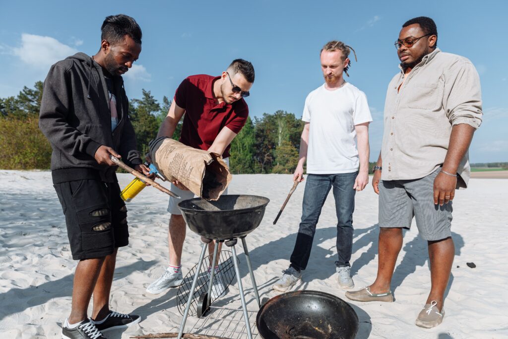 7 Myths Standing Between Men and Their Best Self: Men’s Health Month 4 A group of diverse men preparing a barbecue on a sandy beach under the sun.