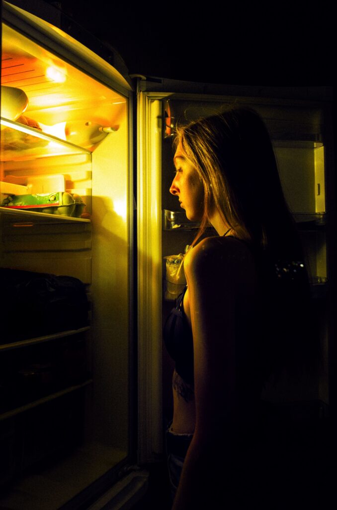 lady stands in front of the fridge at night.
