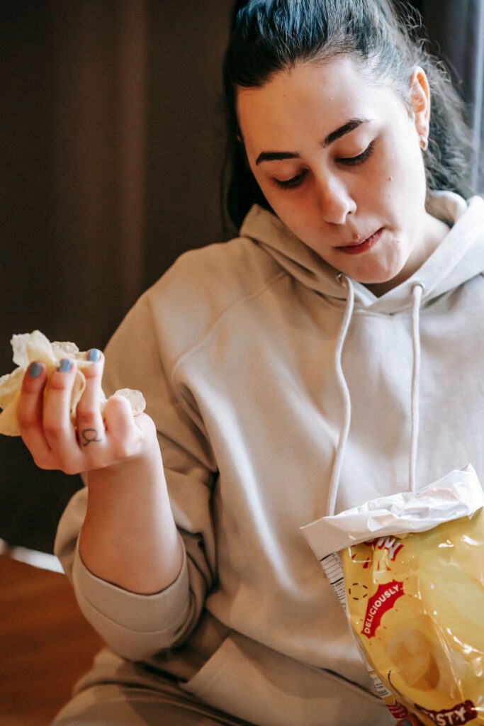 a stressed lady mindlessly eats potato chips wearing a hoodie.  Behavioral Nutrition is the emergent field that takes a multi-disciplinary approach to weight loss
