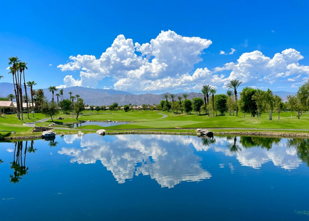 Swing Away: Golf's Secret Role in Weight Loss 1 a beautiful lake sits in front of a golf course which is in front of a mountain in the distance with a deep blue sky and big puffy cumulonimbus clouds